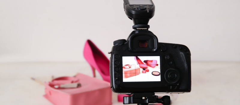 Fashionable shoes, bag and cosmetics on display of professional photo camera in studio